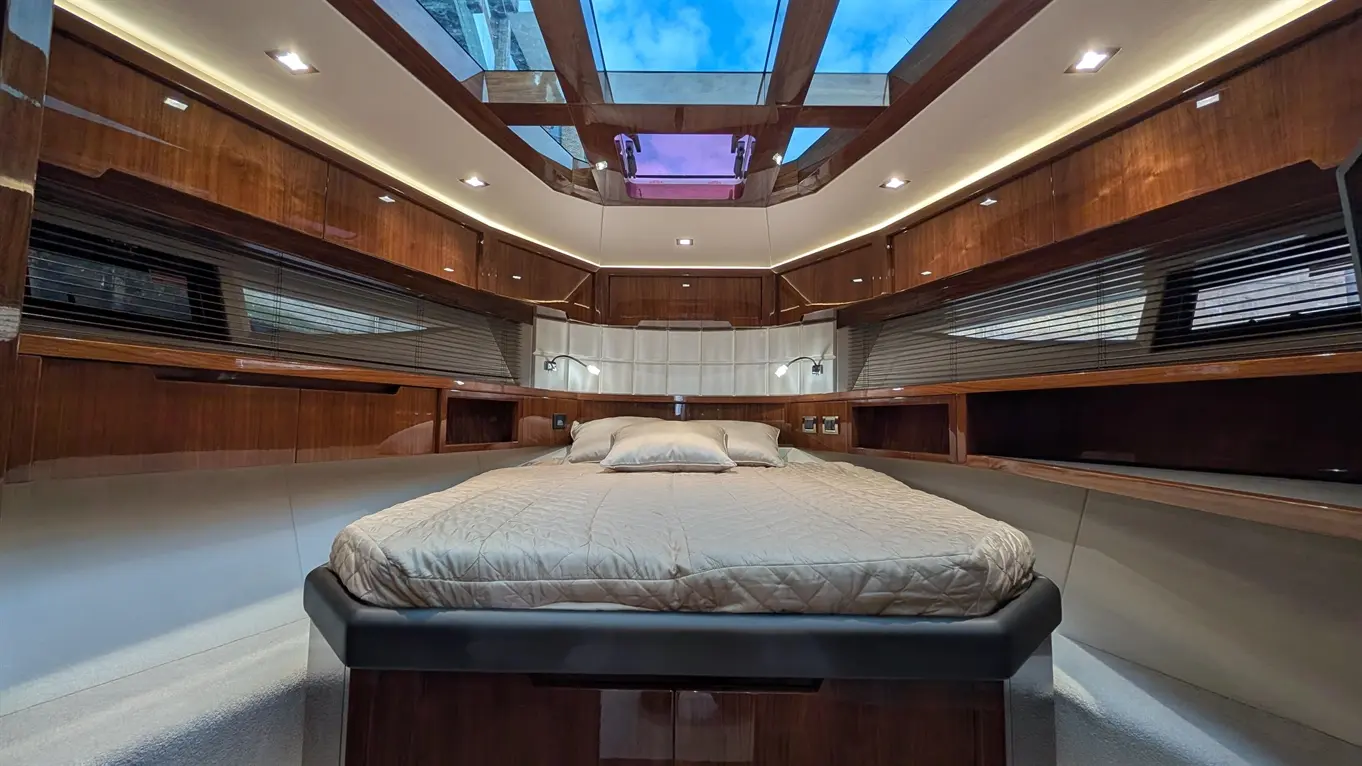 Interior of a luxury yacht cabin featuring a queen-sized bed, wooden cabinetry, and a skylight with blue skies visible.